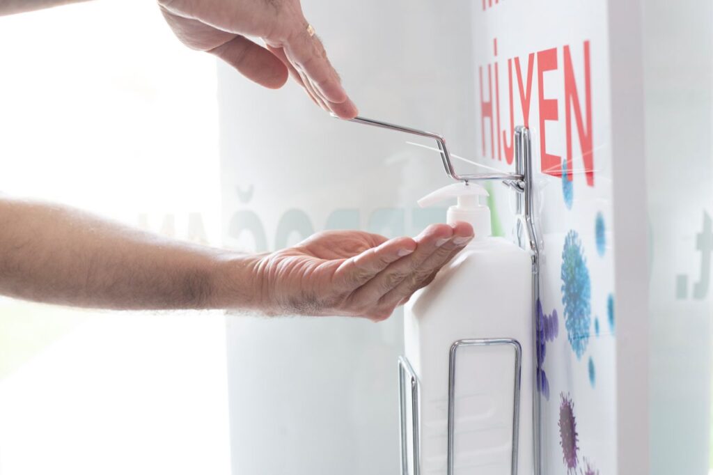 Close-up of hands using a liquid disinfectant dispenser in a clean environment emphasizing hygiene.