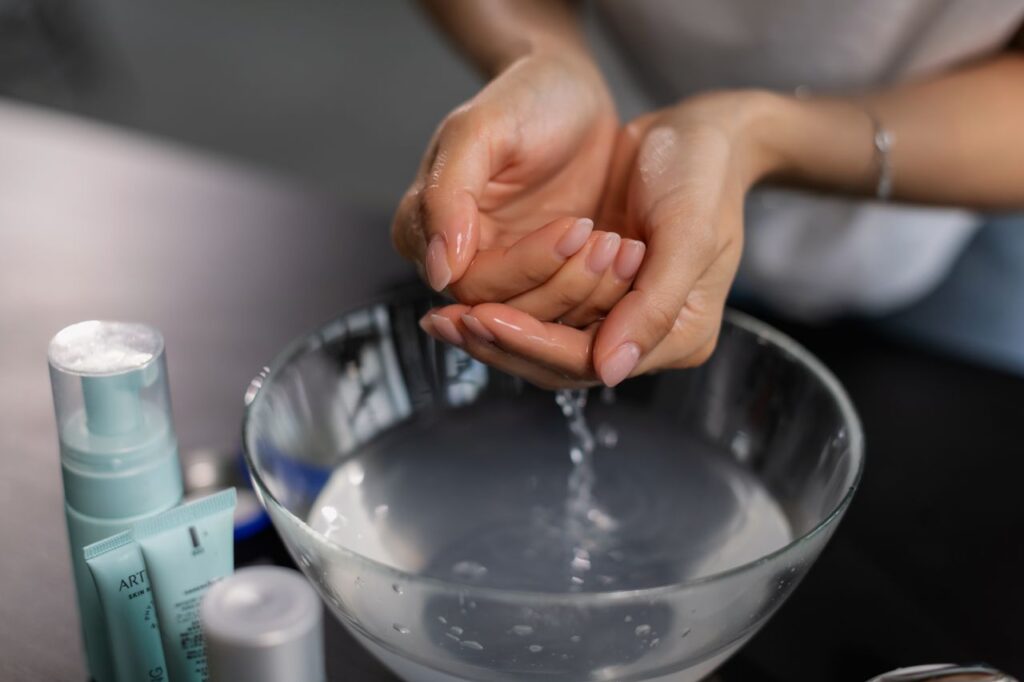 Close-up of hands in skincare routine with hydrating products and water bowl.